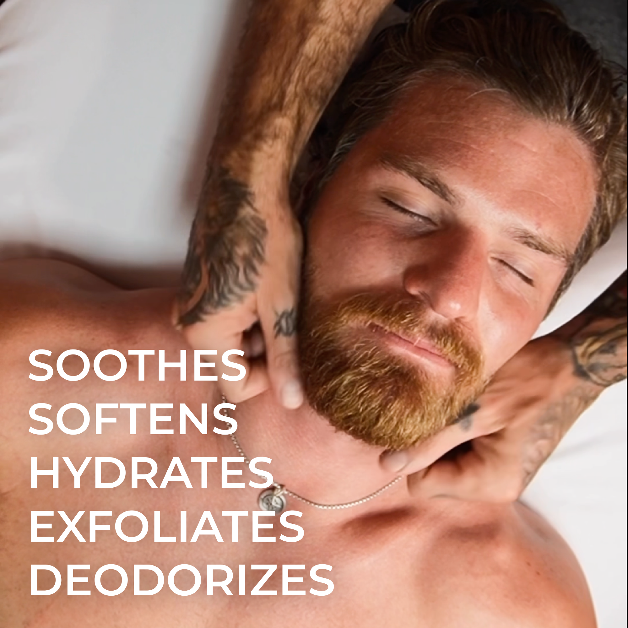 Man with a beard and tattoos lying down, receiving a beard oil application with text about skincare benefits.